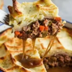 A serving of Shepherd's Pie with mashed potatoes and hearty meat and vegetable filling being lifted by a fork.